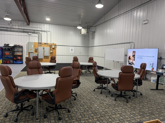 Sharalife first aid classroom with round tables, rolling chairs, whiteboard, and presentation screen
